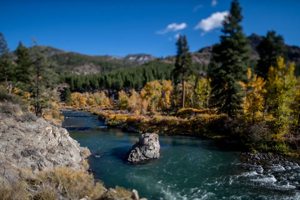 Blue river water curves between rocks and autumn trees.