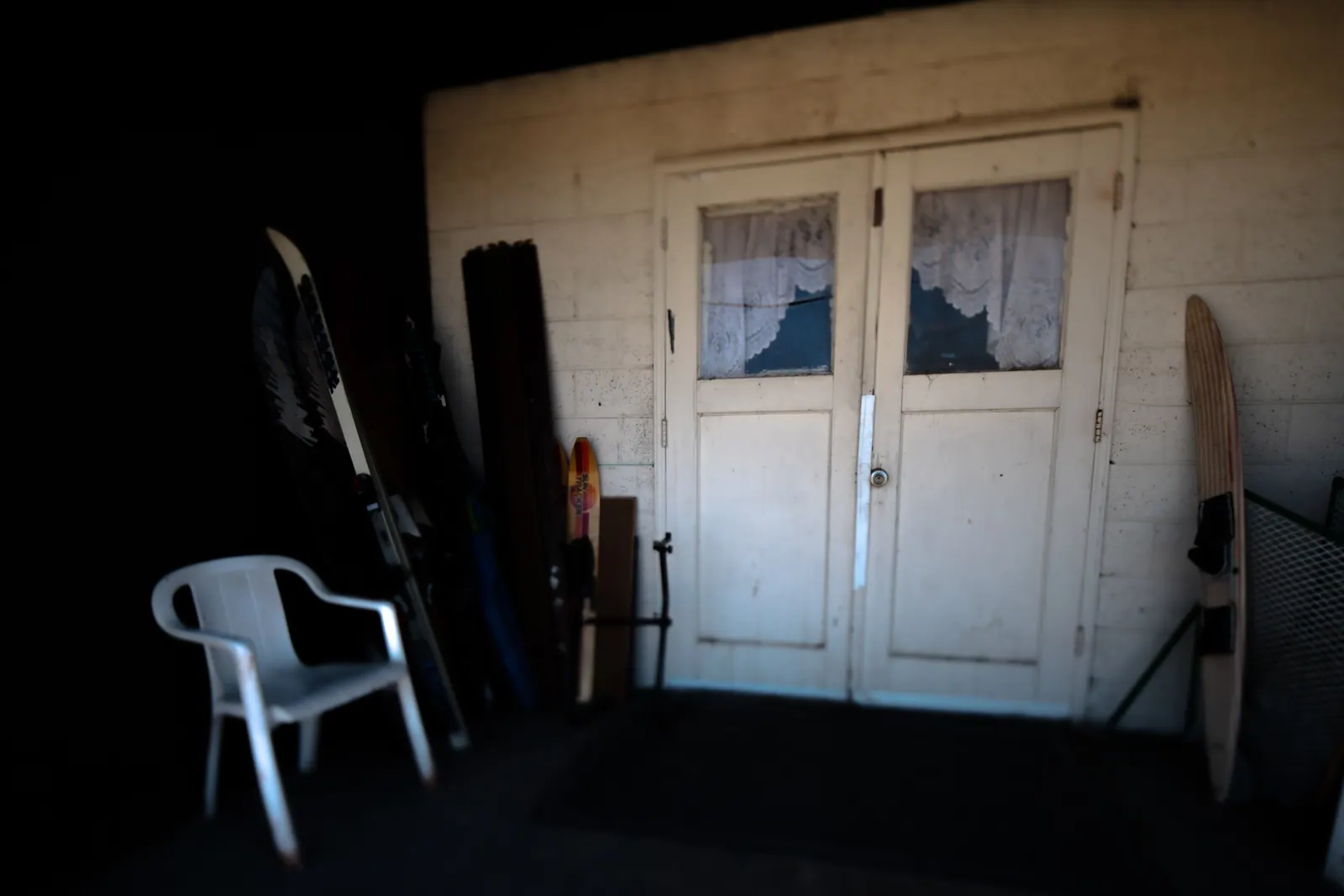 A white plastic chair waits beside closed double doors inside a dark room.