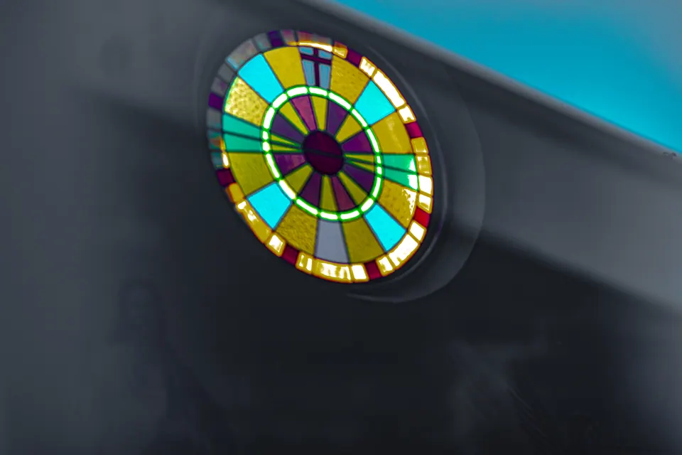 Light passes through a round stained-glass window set in a pale wall.