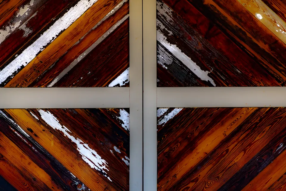 Pale beams divide diagonal boards covered in peeling red and white paint.