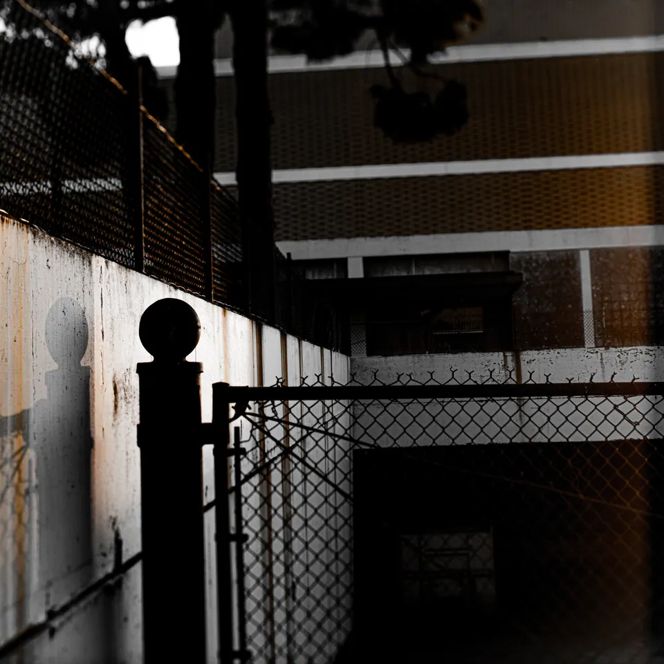 Railings and a chain-link fence divide a starkly lit passage into geometric shapes.