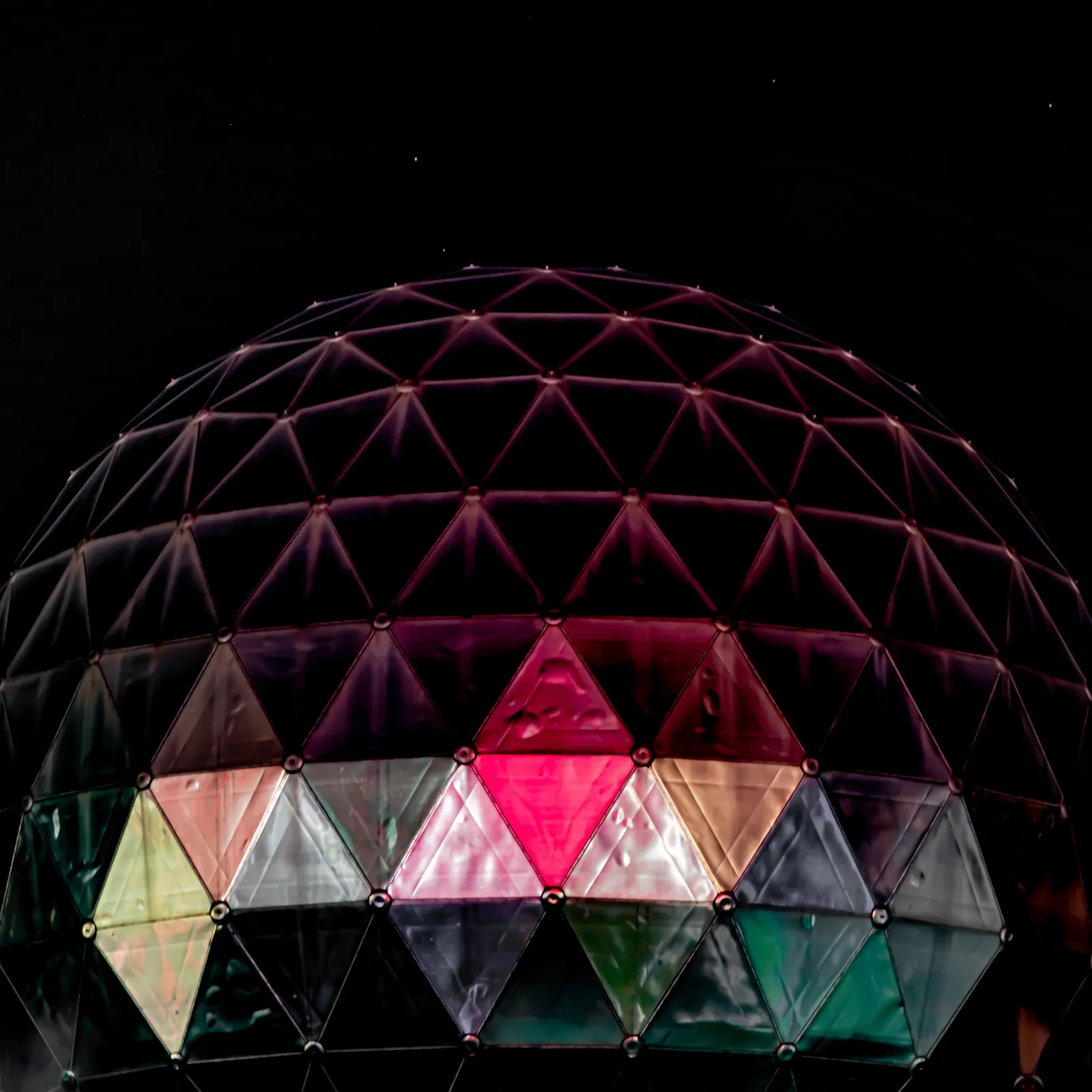 Coloured triangular panels form a glowing dome against the night sky.