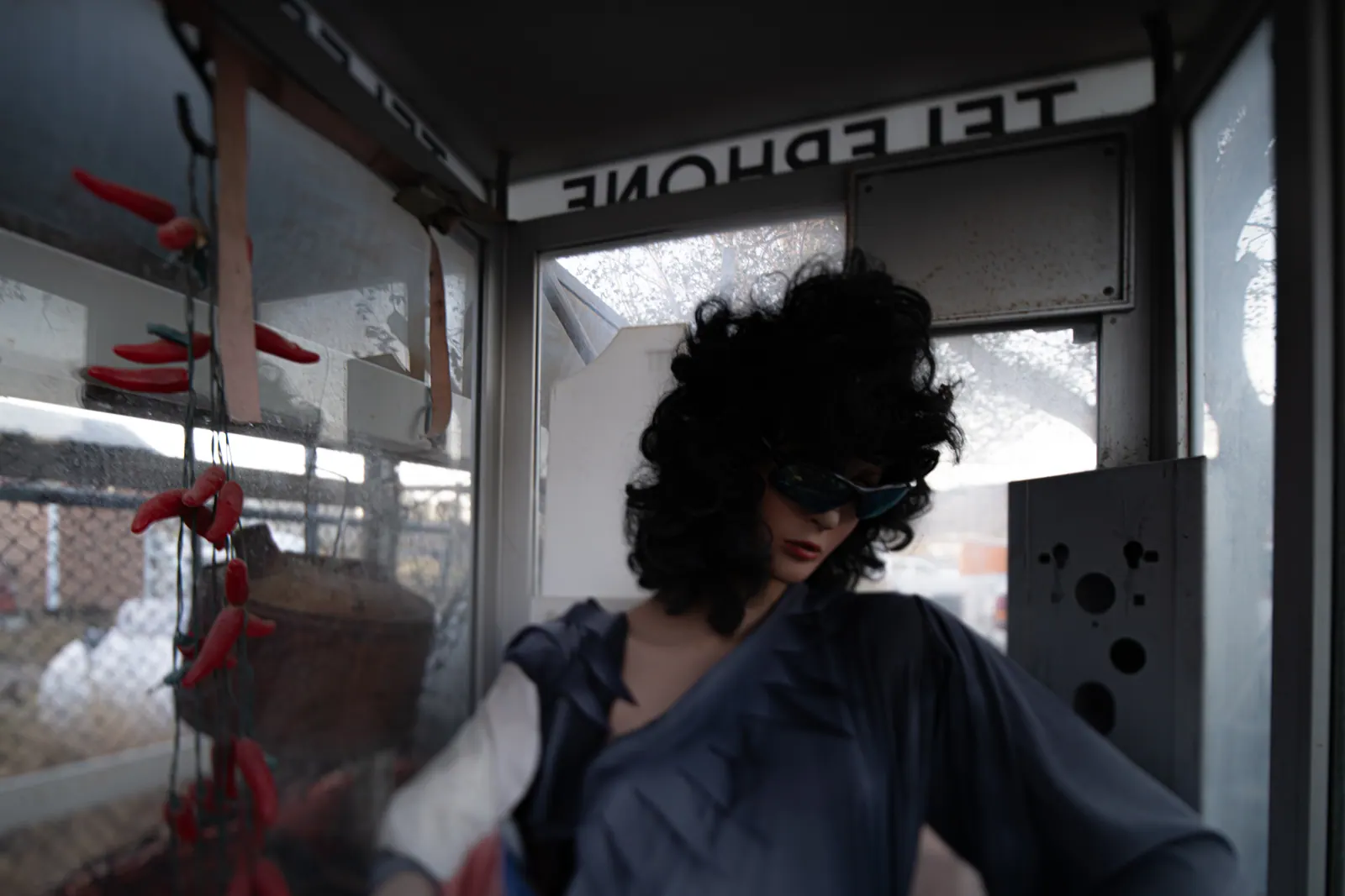 A mannequin in dark glasses occupies a weathered telephone booth.
