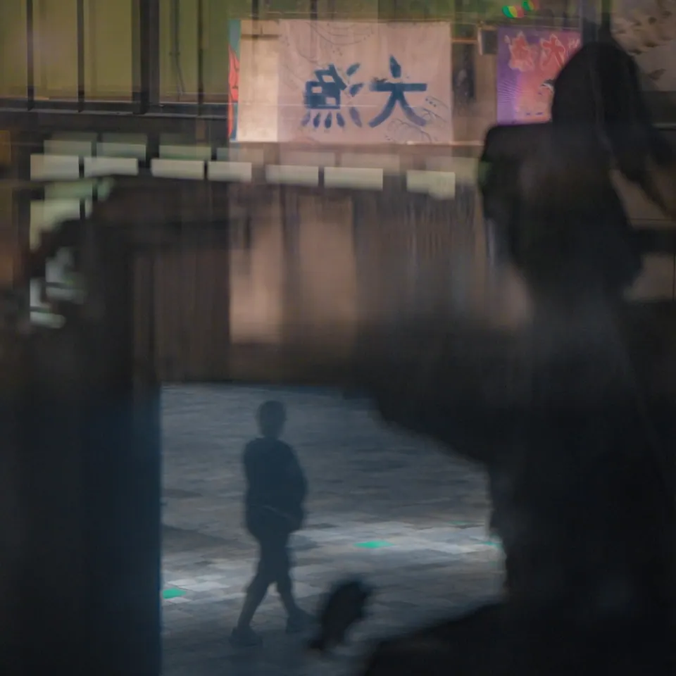 A walking figure appears through layered reflections in a city window.