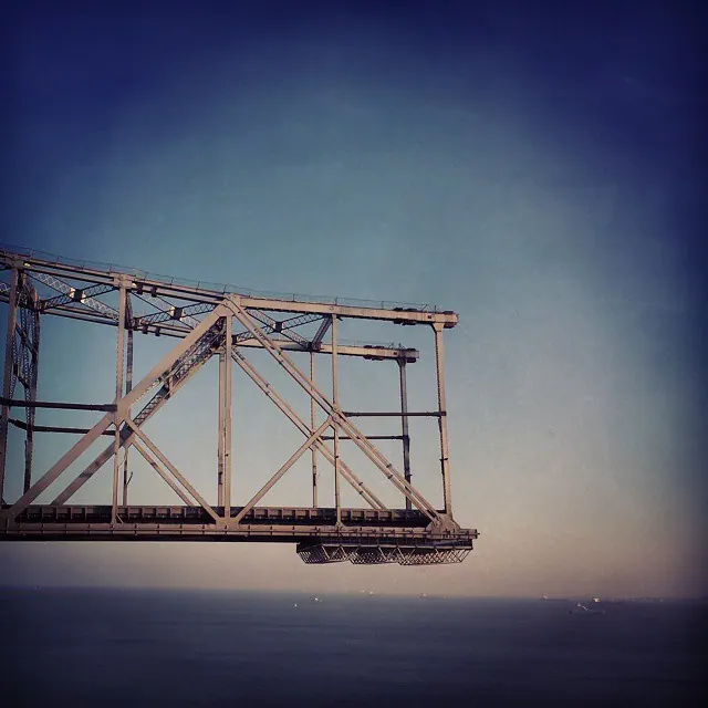 A pale rectangular metal frame hangs above flat blue water beneath a clear sky.