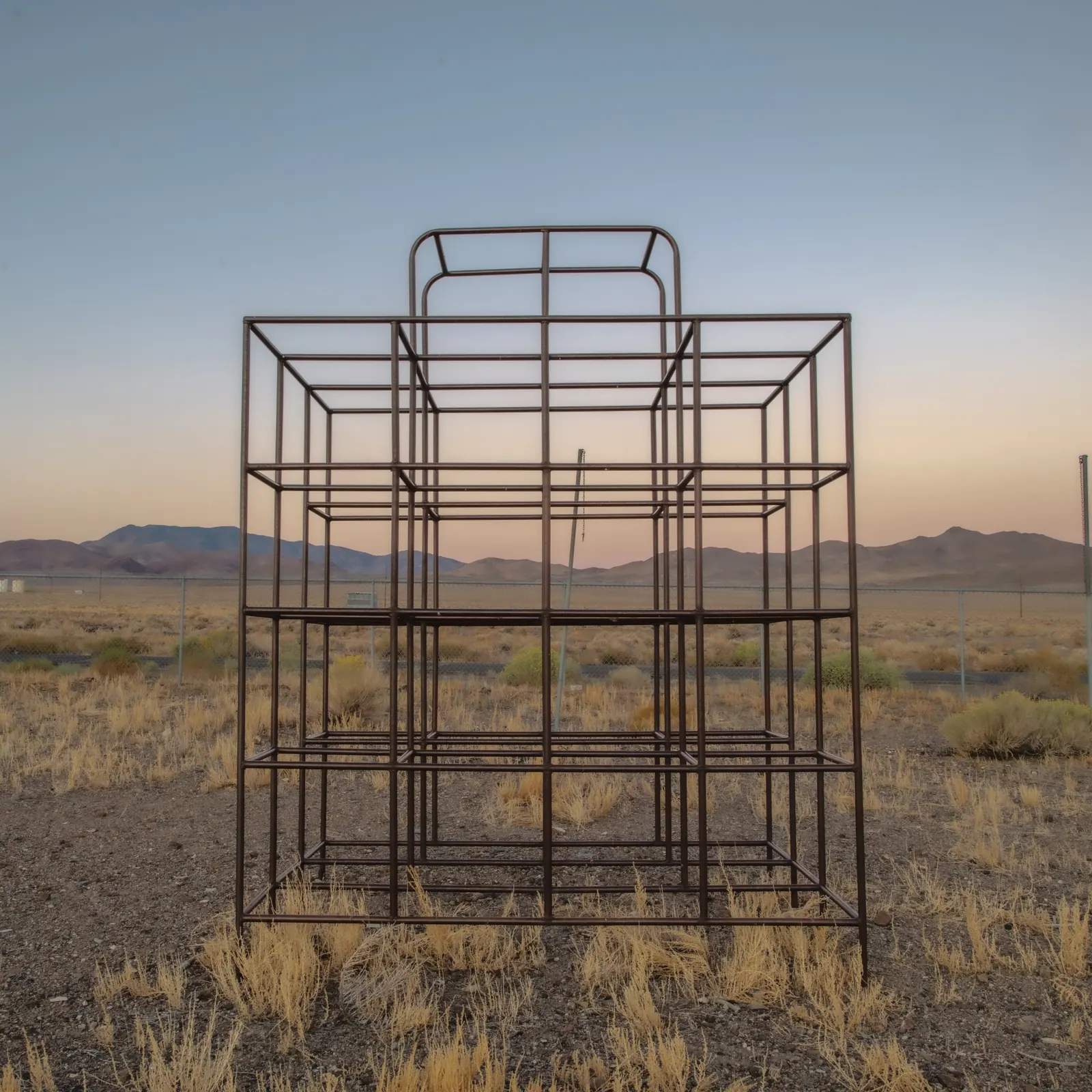 An empty metal frame stands alone in dry grass beneath a pale evening sky.