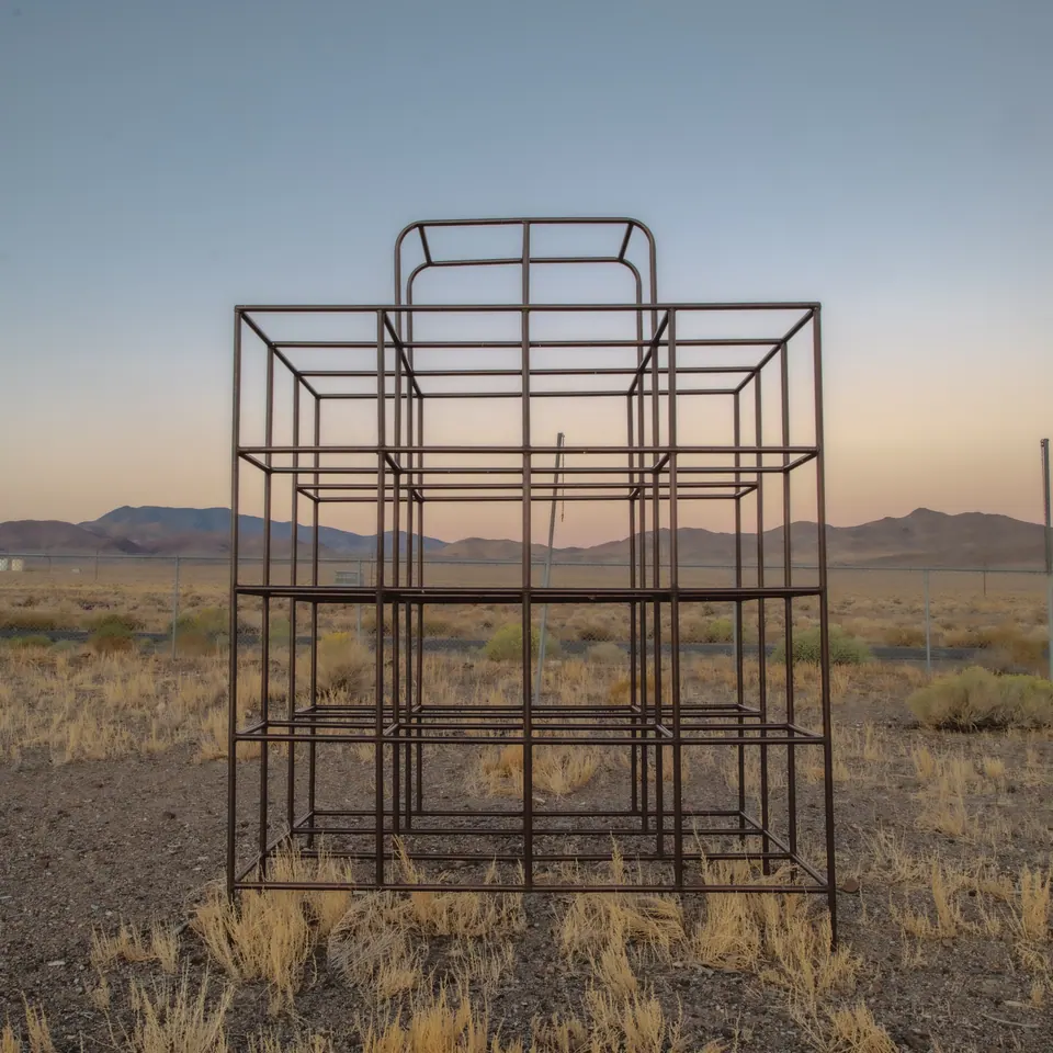 An empty metal frame stands alone in dry grass beneath a pale evening sky.