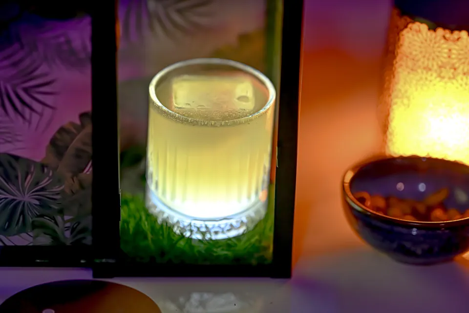 A pale green drink glows among warm lamps and rich colours on a table.