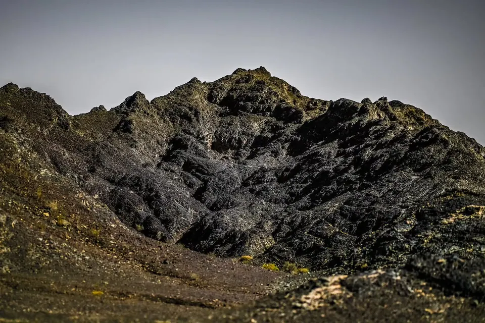 Dark, sharply folded mountain ridges rise beneath a pale blue sky.