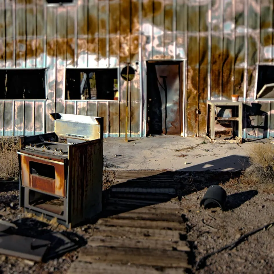 An abandoned stove sits outside a patchwork building of timber and metal.