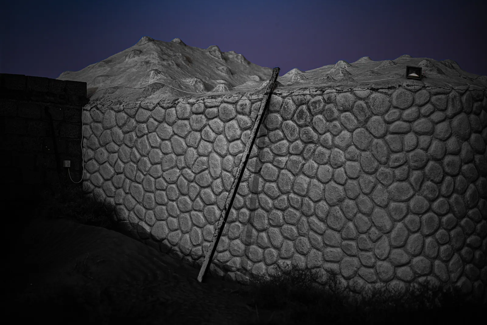 A wooden ladder leans against a textured stone wall beneath a blue evening sky.