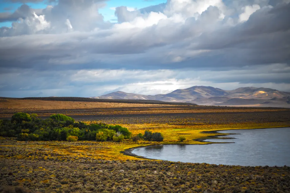 A band of blue water meets golden ground beneath layered grey clouds.