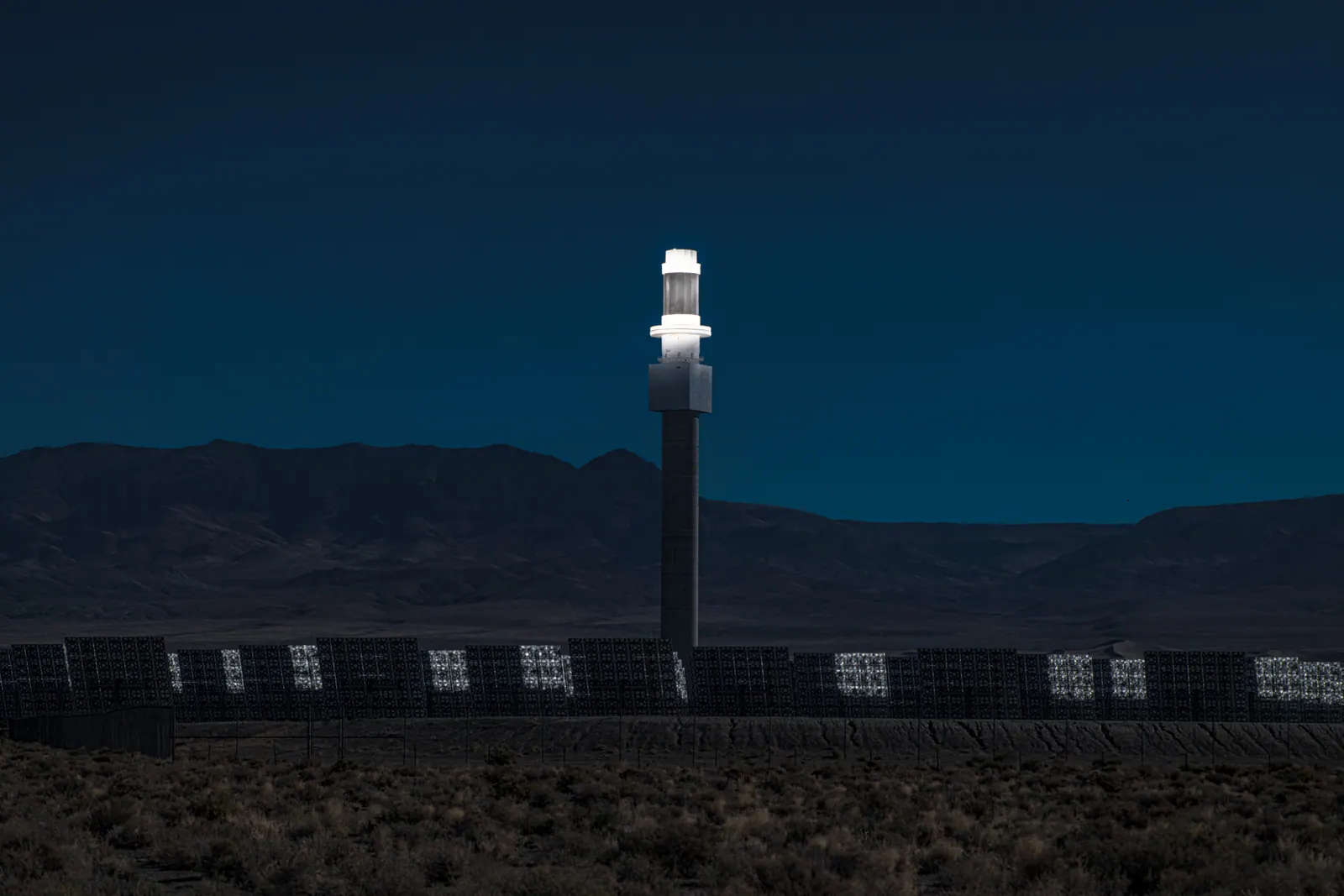 A tall, bright white tower stands against a deep blue sky and distant desert mountains.