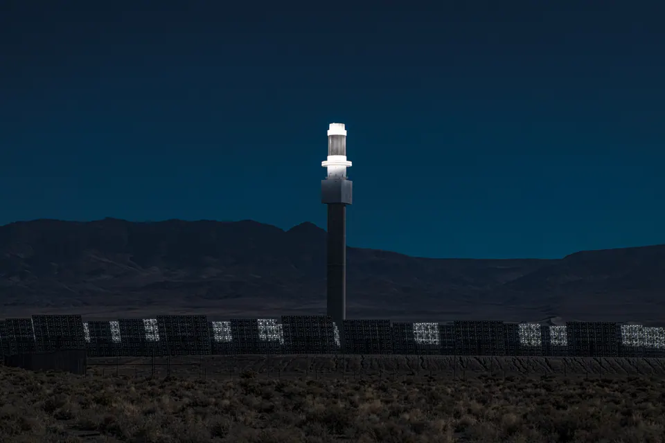 A tall, bright white tower stands against a deep blue sky and distant desert mountains.
