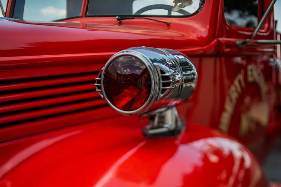 A polished metal lamp projects from the bright red body of an old vehicle.