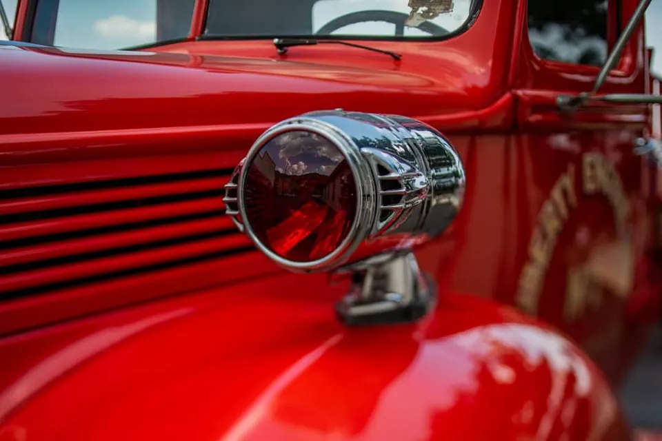 A polished metal lamp projects from the bright red body of an old vehicle.