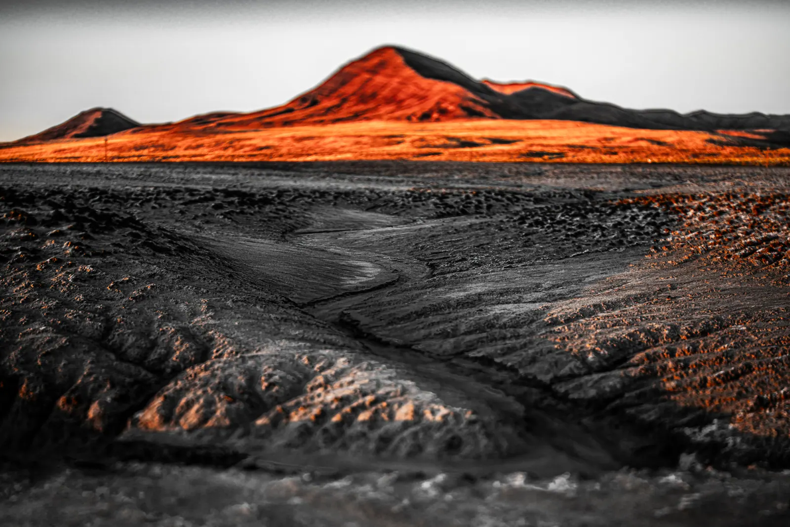 A rust-red hill catches the light above a grey, deeply textured desert foreground.