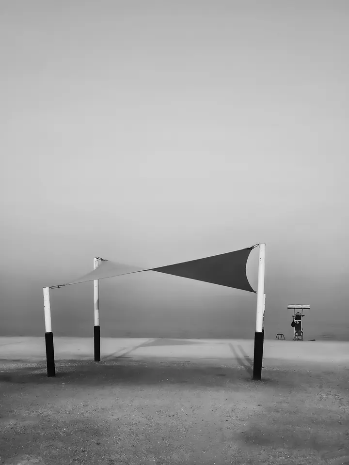 A stretched fabric shade canopy stands alone in a hazy, nearly featureless landscape.