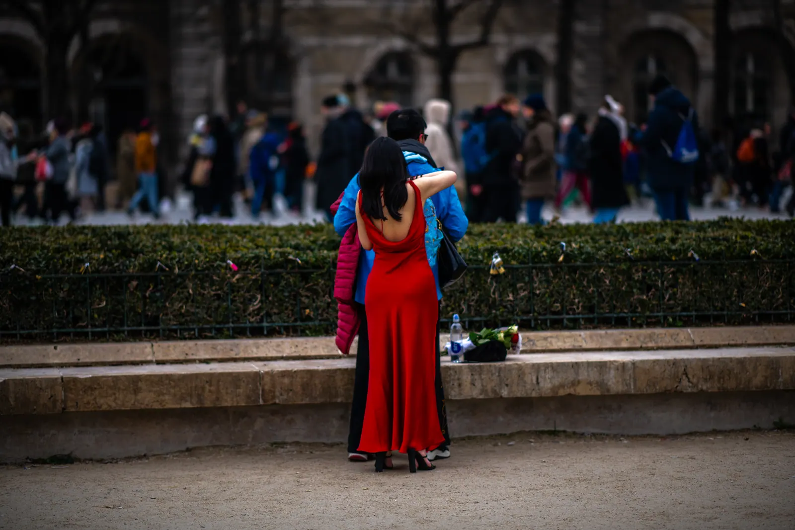 A person in a long red garment stands apart from a crowd outside a cathedral.