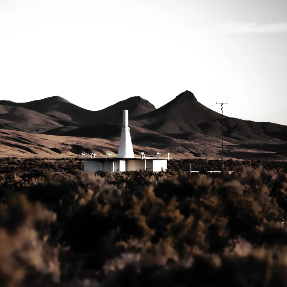 A white tower stands against dark mountains beyond a foreground of desert brush.