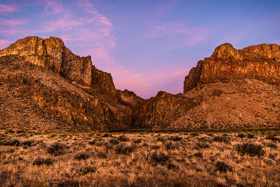 A pink evening sky opens between two rugged desert rock formations.