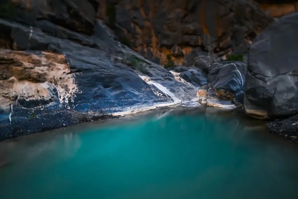 Turquoise water gathers in a smooth, grey rock basin.
