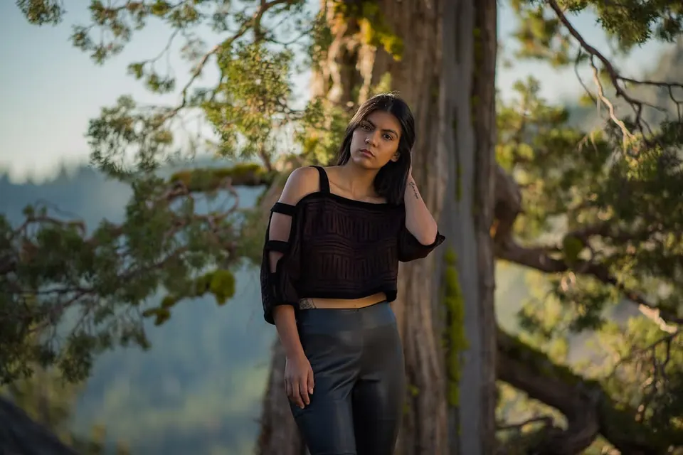 A person in a dark top stands beside a tree in soft outdoor light.