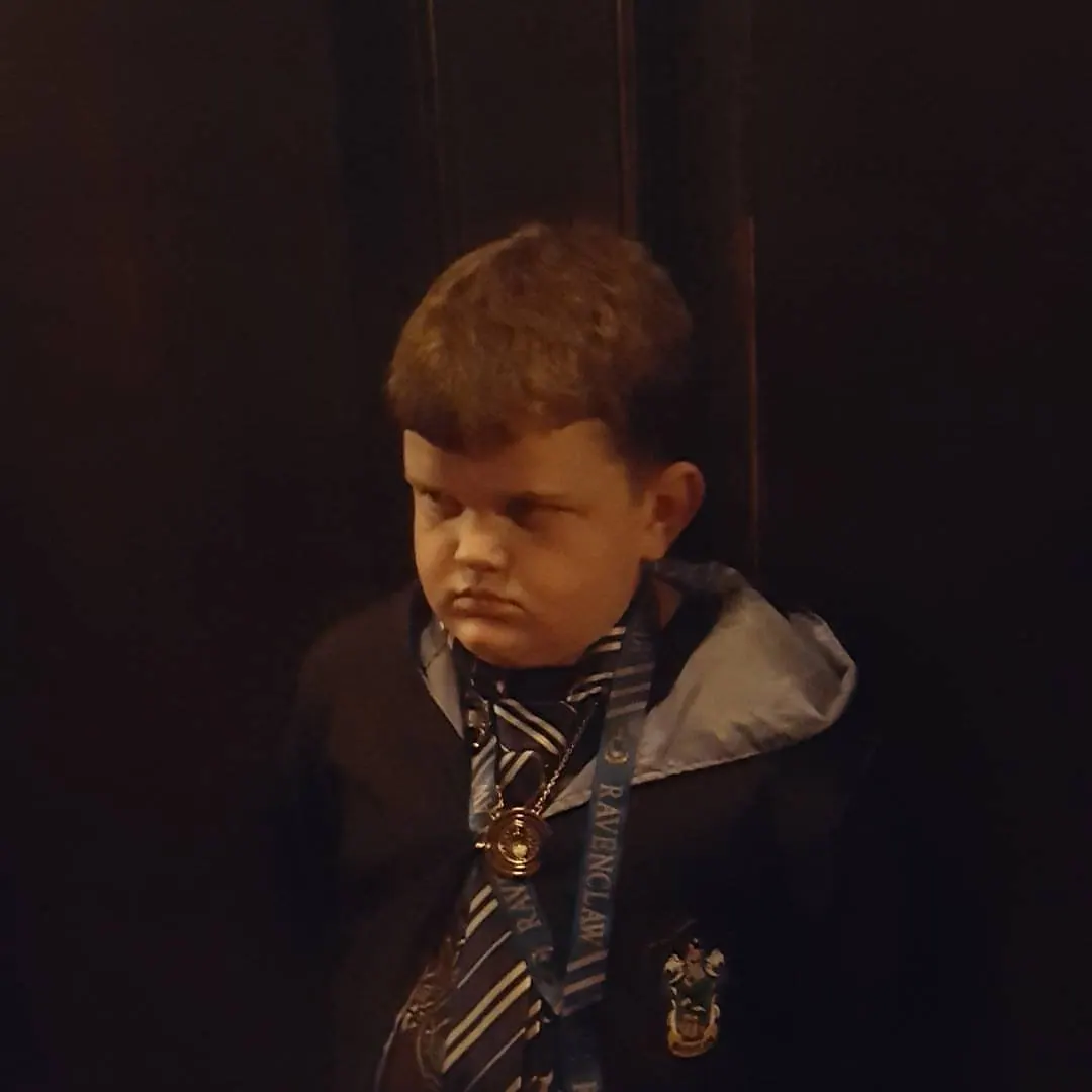 A young person in a jacket stands against a dark, warmly lit background.