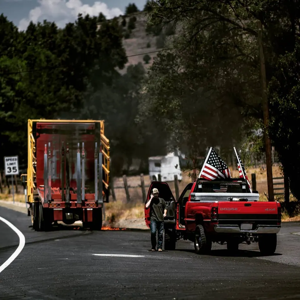 Vehicles and flags move along a small road bordered by trees.