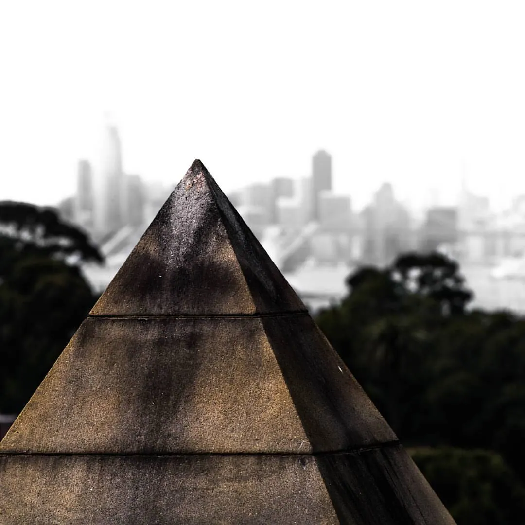 A pointed stone monument rises in front of a softly blurred city skyline.