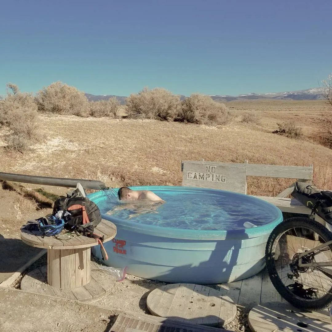 A bicycle and small objects rest beside a round outdoor pool in dry country.
