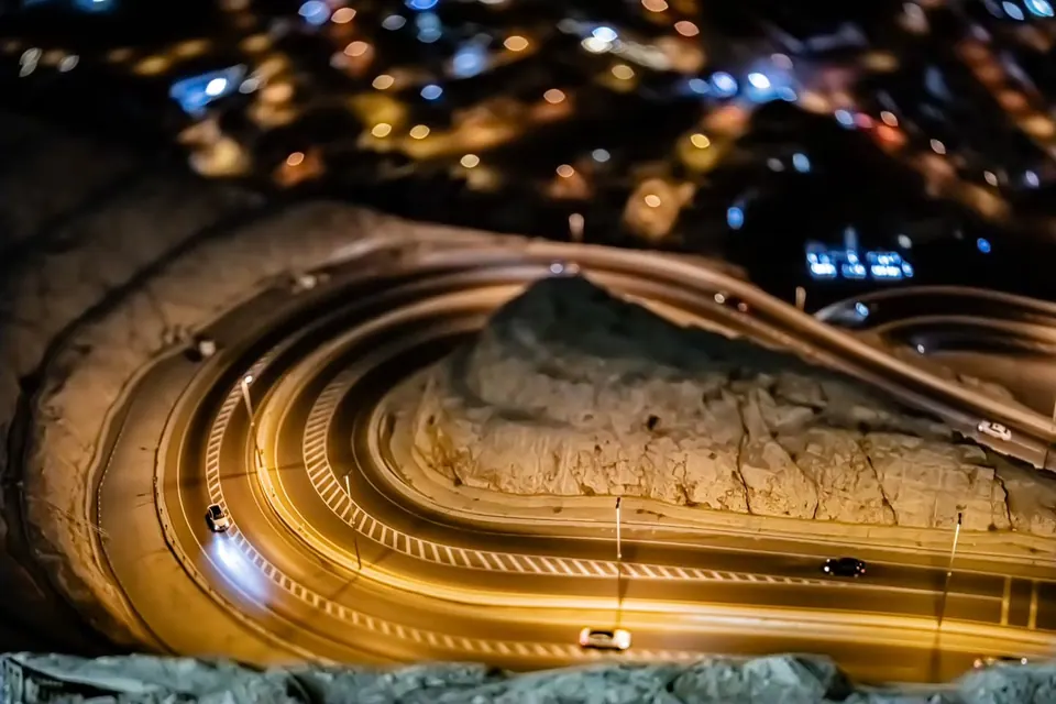 Light trails follow a winding road through the hills at night.
