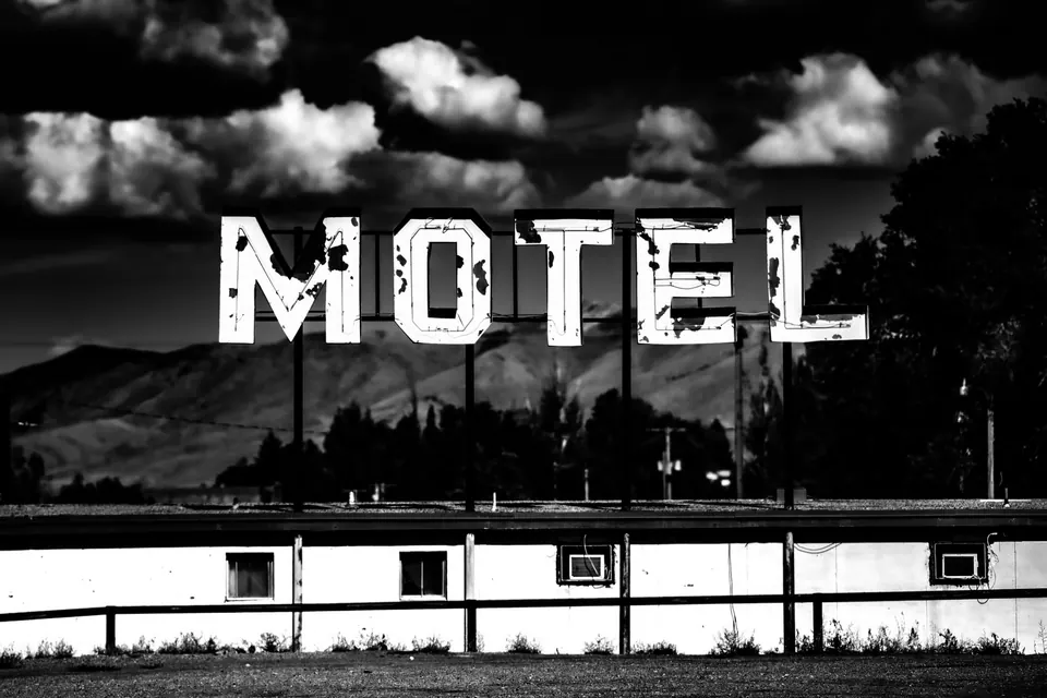 Large letters spelling MOTEL rise over a low roadside building under dramatic clouds.