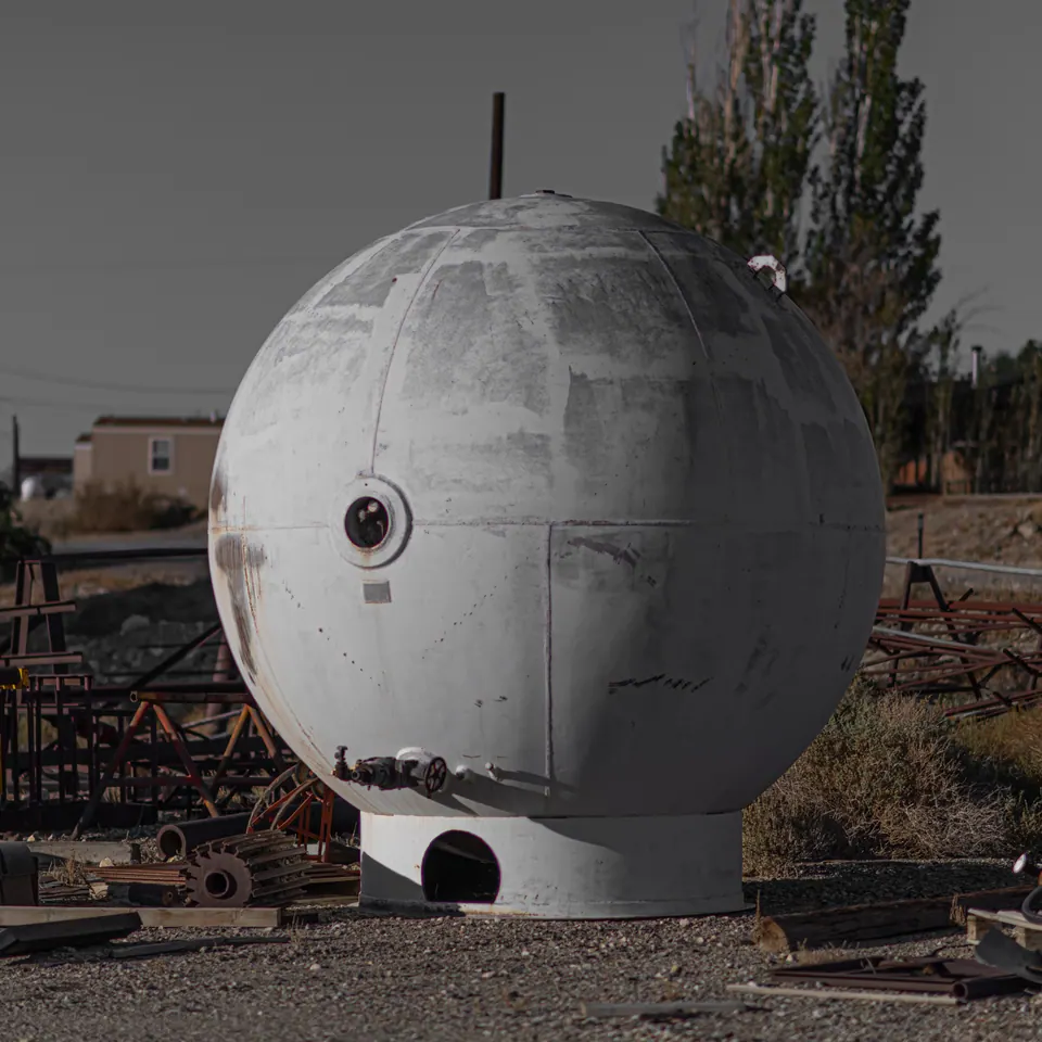 A large white spherical structure stands among industrial objects in a desert town.