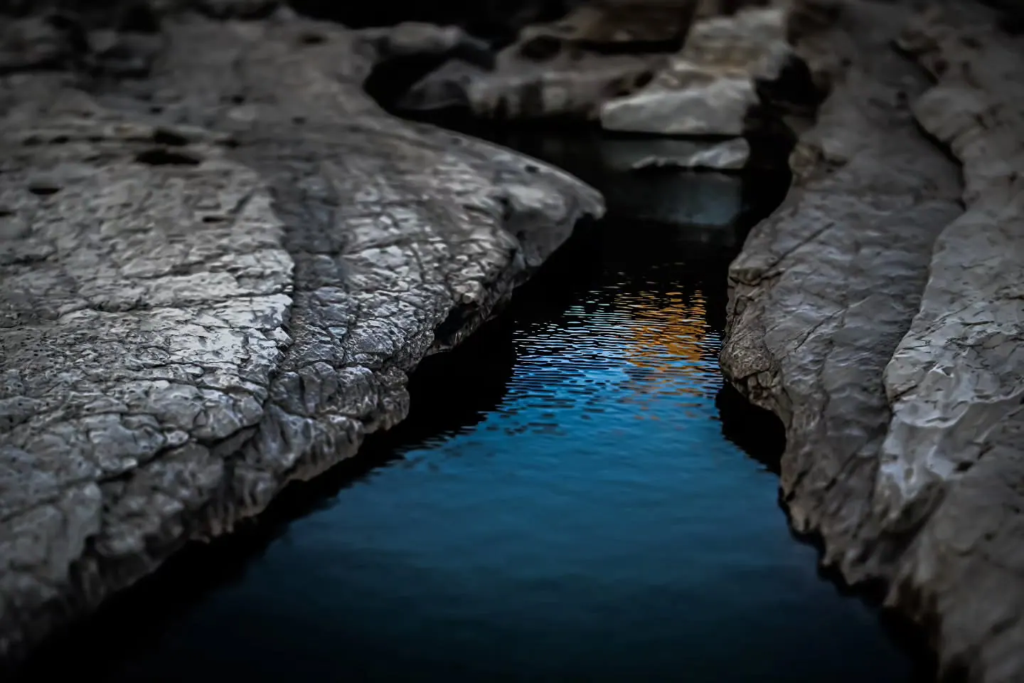 Blue water follows a narrow fissure between smooth grey rocks.