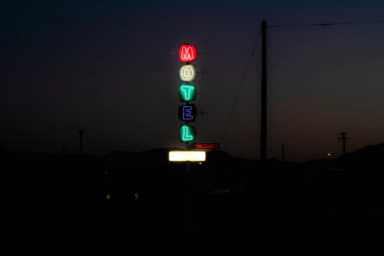 Vertically stacked MOTEL letters glow in red, green and blue against the evening sky.