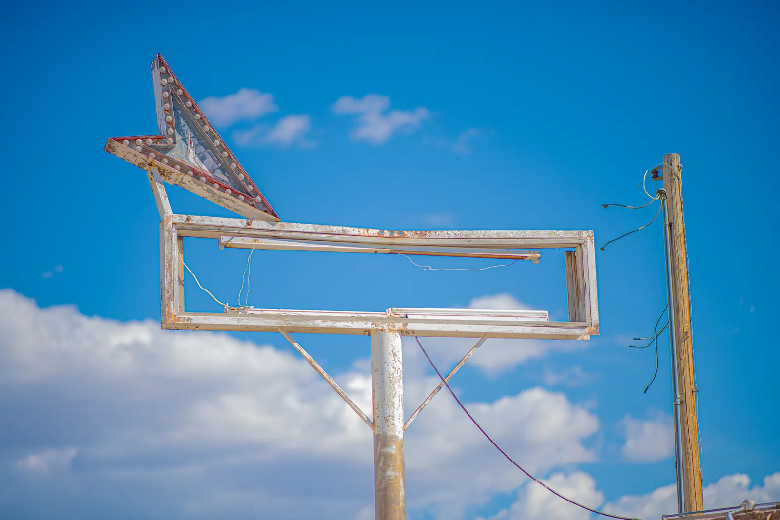 A faded arrow and empty sign frame stand against a bright blue sky.