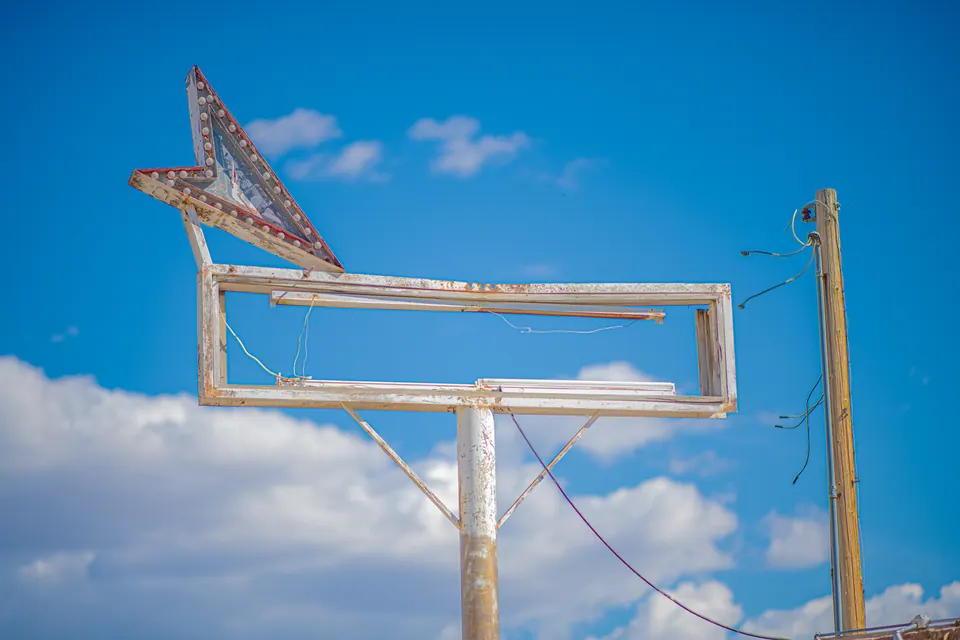A faded arrow and empty sign frame stand against a bright blue sky.