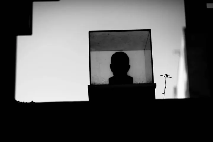 A dark figure appears within a rectangular frame against a pale gallery wall.
