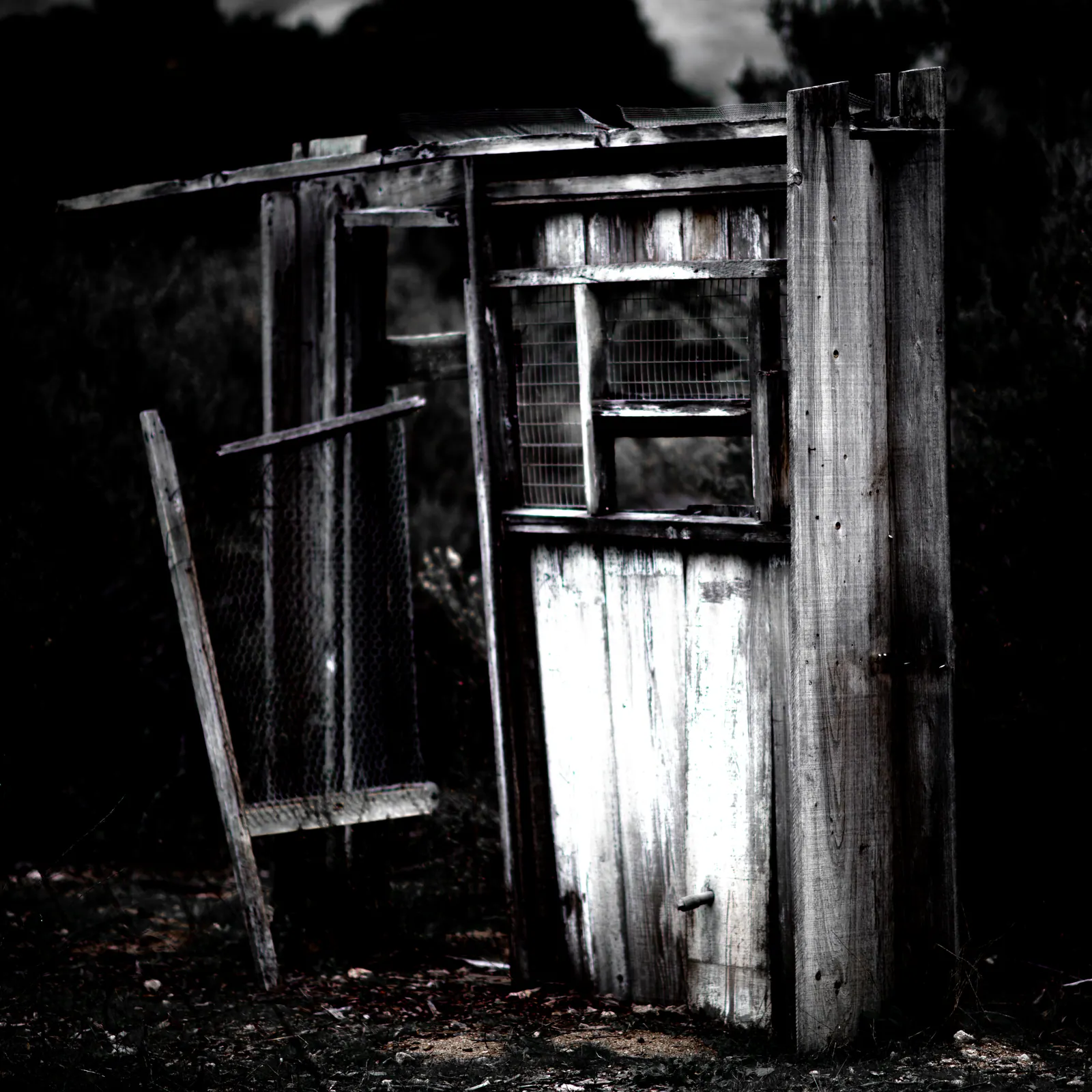 A weathered wooden enclosure leans into deep shadow among rough boards.