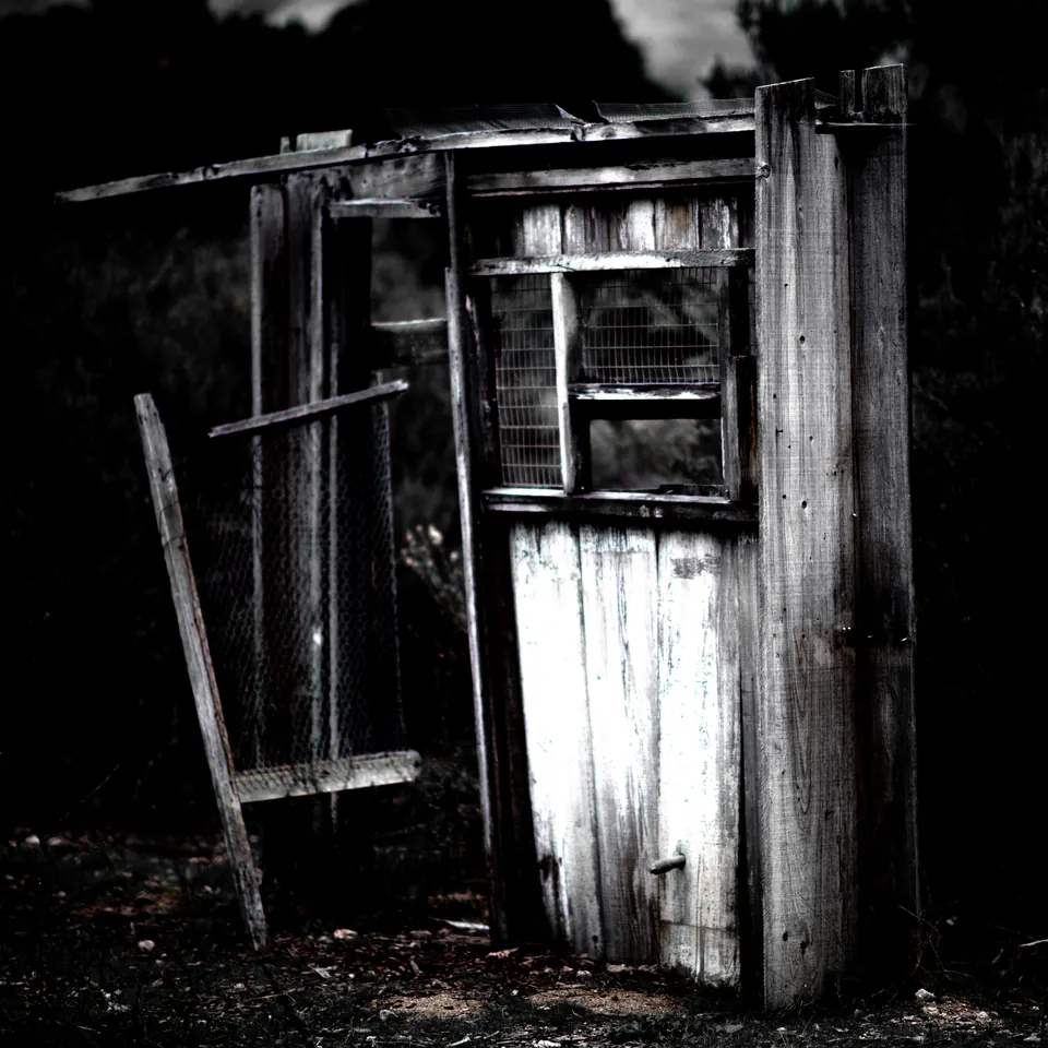 A weathered wooden enclosure leans into deep shadow among rough boards.
