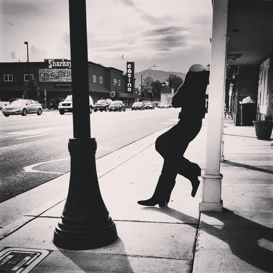 A silhouetted figure moves past a street post into bright sunlight.