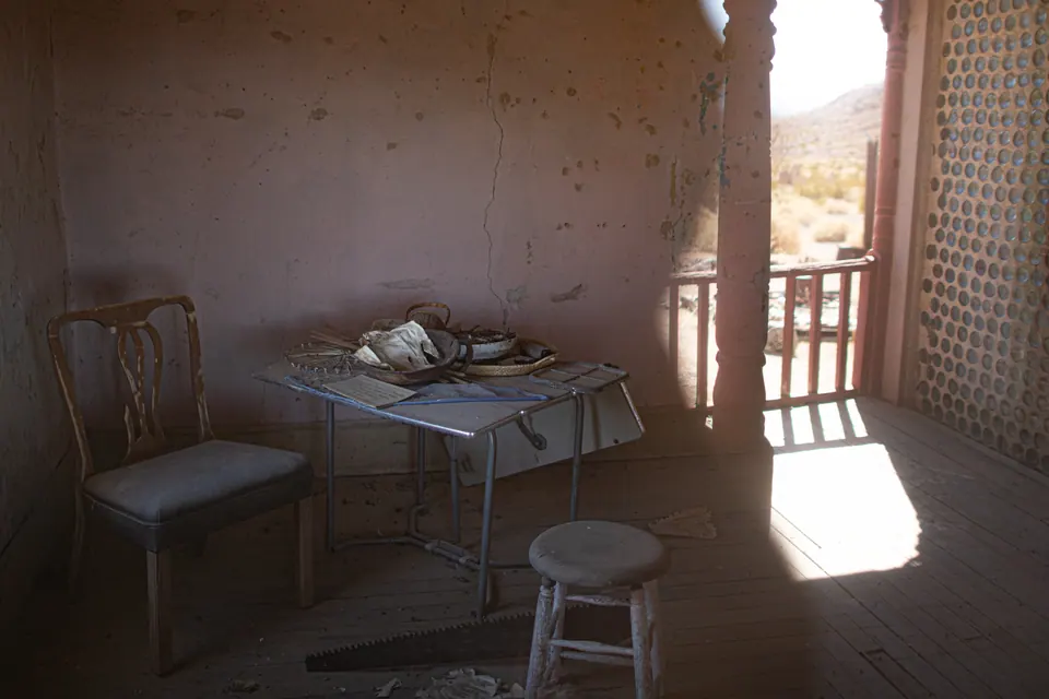 A table and chairs remain in an empty room lit through an open doorway.