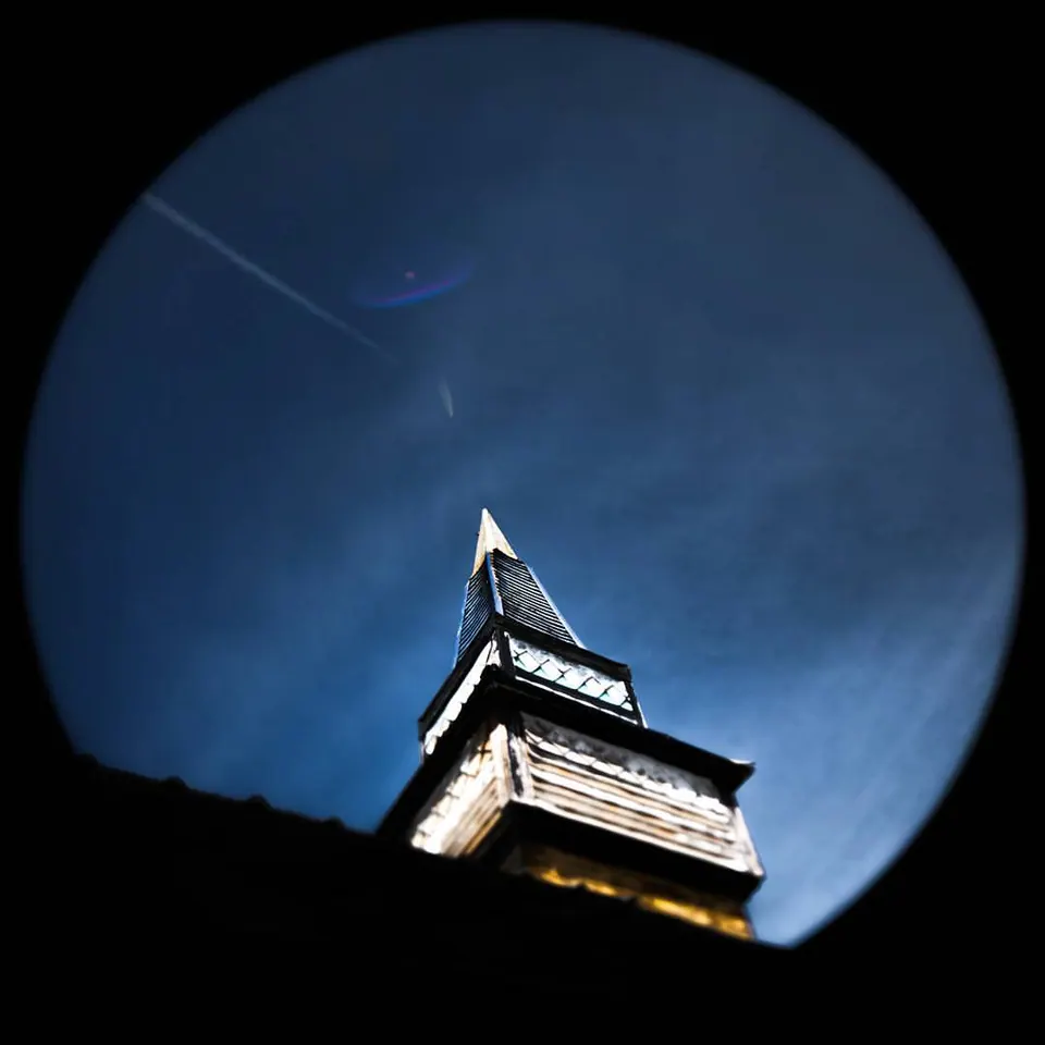 A pointed building roof appears within a round blue opening against deep shadow.
