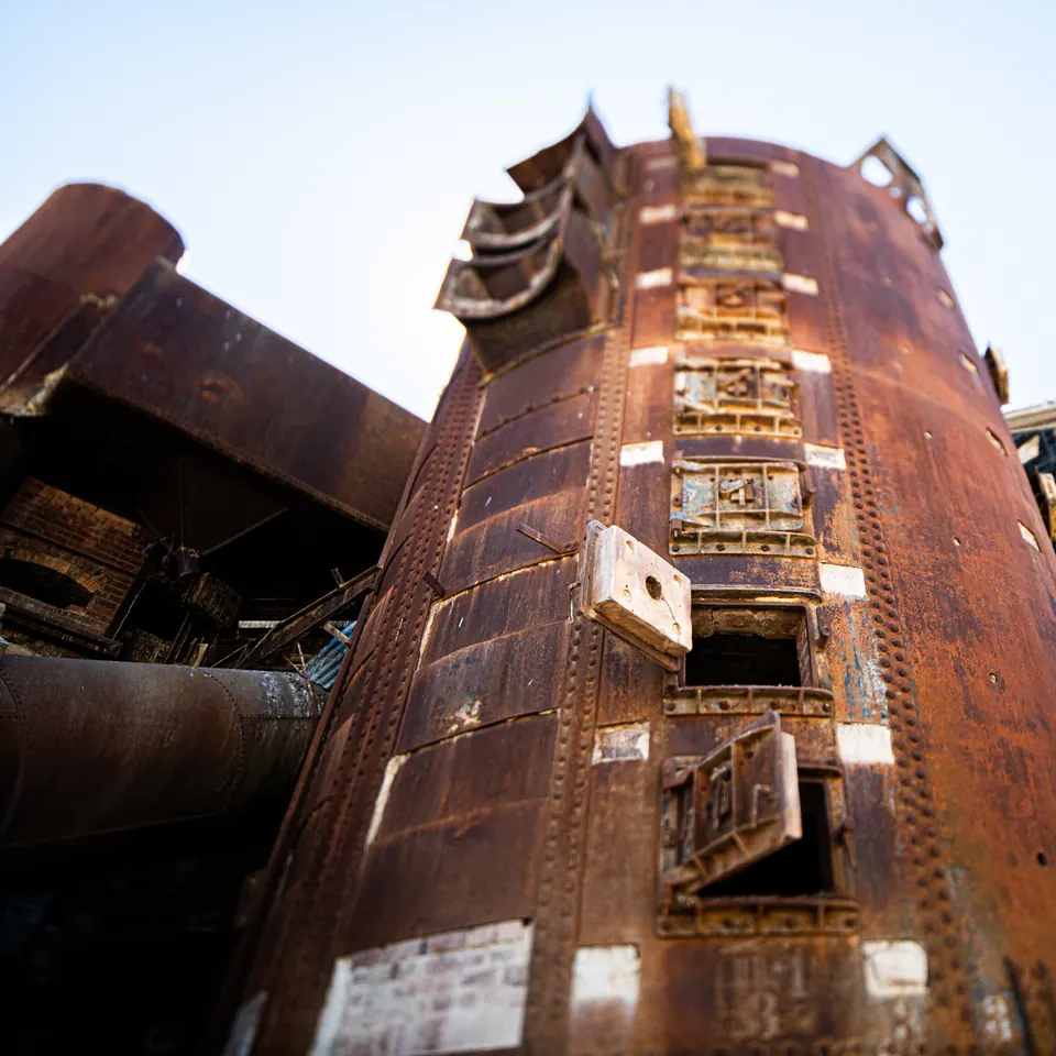 A rusted industrial tower rises into a pale sky, lined with ladders and platforms.
