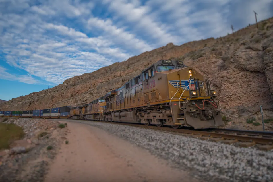 A yellow locomotive pulls a long line of carriages below a dry hillside.