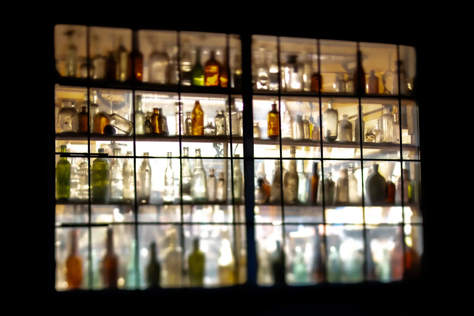 Rows of bottles glow behind a grid of dark window frames.