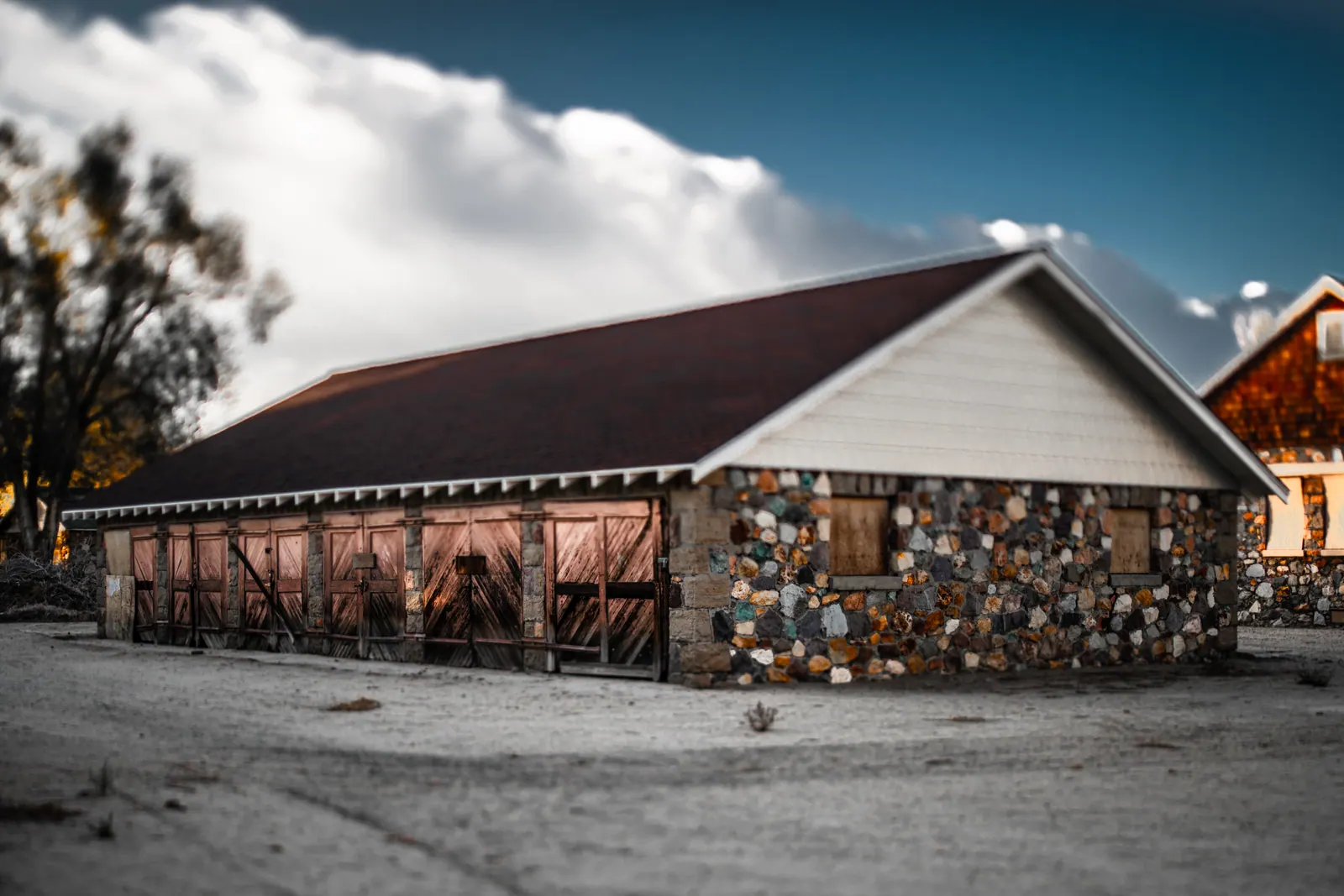 A low building combines a simple roof with a wall of many different stones.