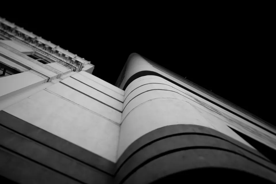 A curved white building edge rises into deep shadow in black and white.