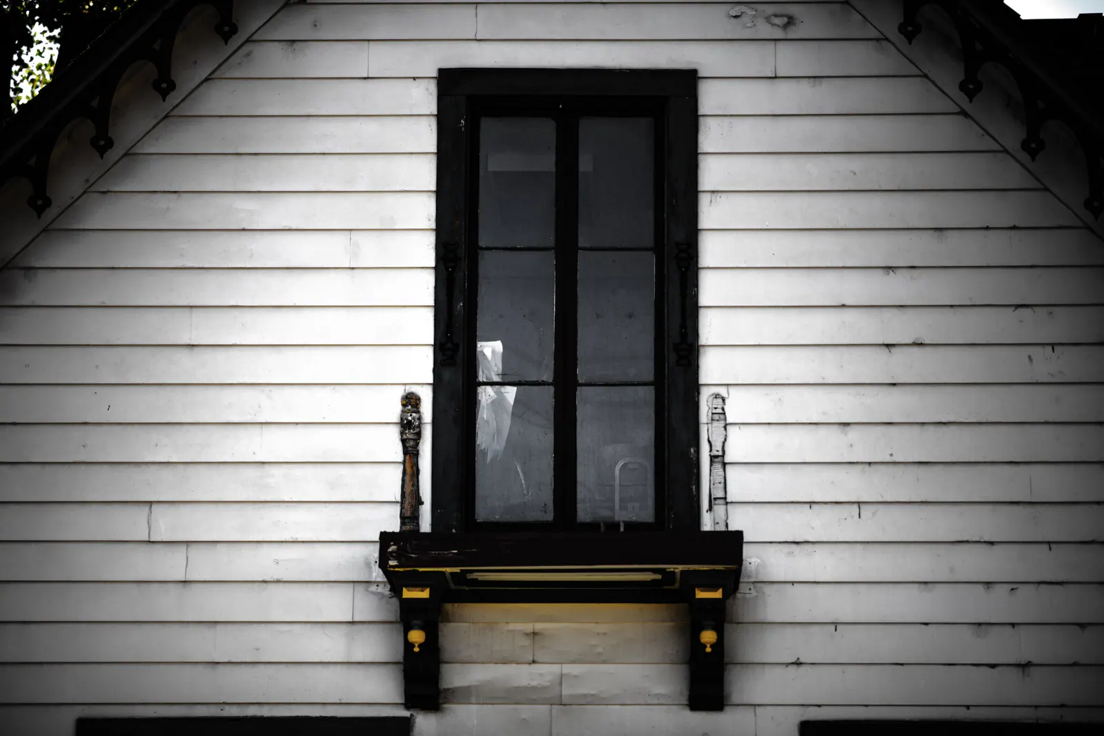 A single dark window sits in a white clapboard wall below a pitched roof.